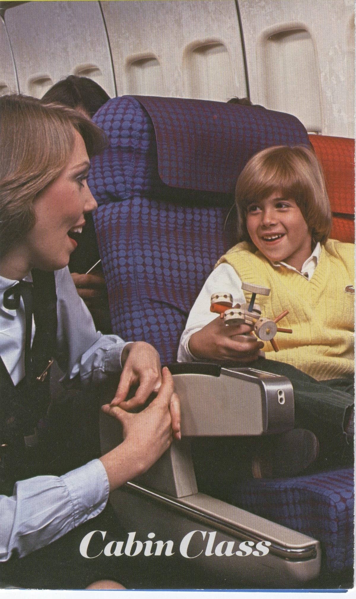 1980s A Pan Am Flight Attendant speaks with a young customer in the economy section of a 747.